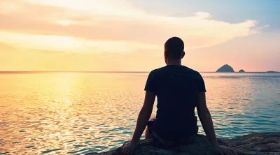 Man sitting on a beach, watching a sunset