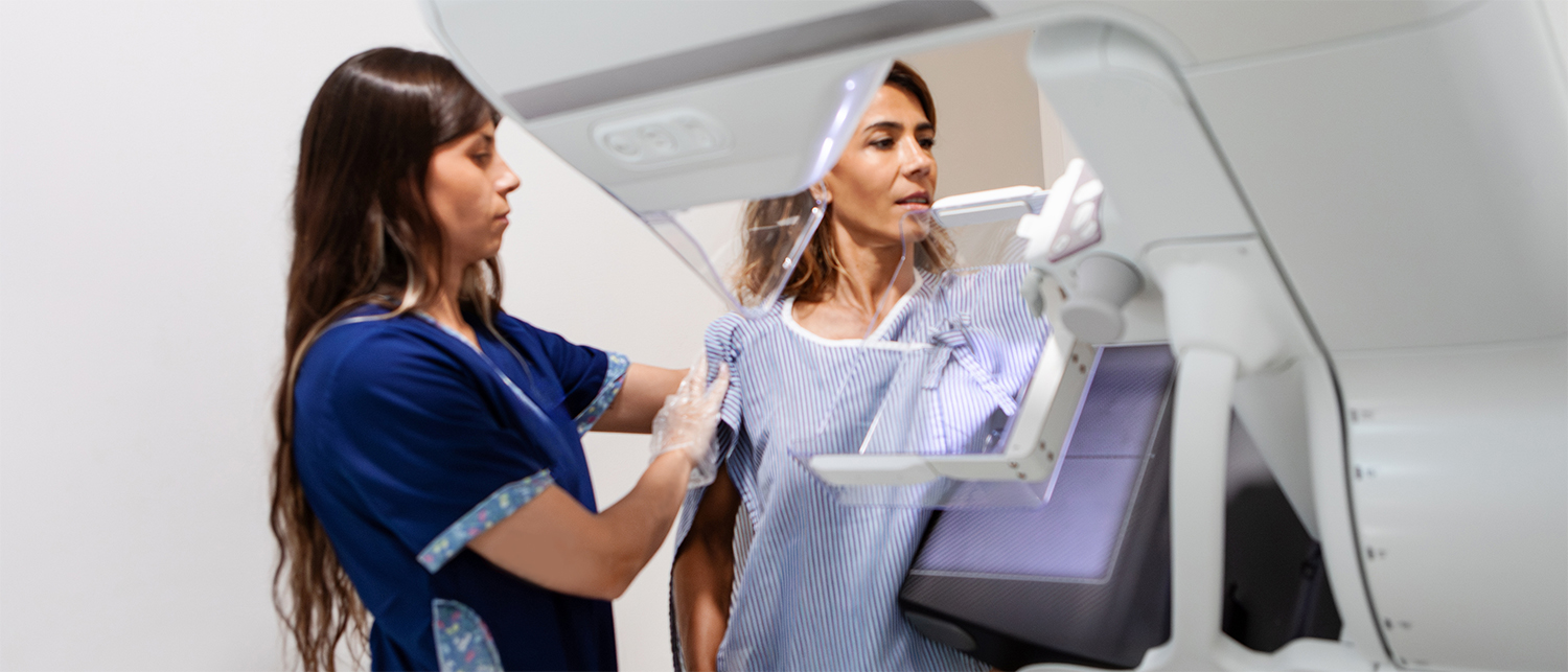 A healthcare worker assists a woman during a preventive screening (mammogram) using a medical imaging machine.