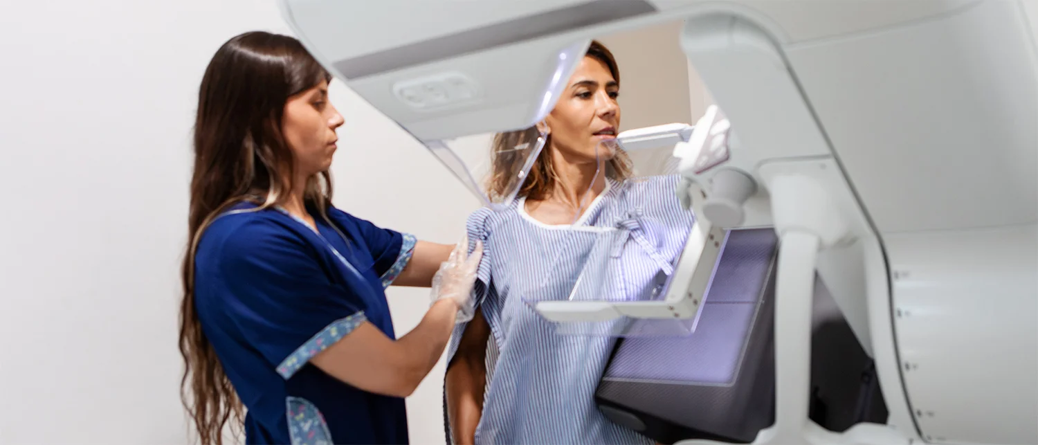 A healthcare worker assists a woman during a preventive screening (mammogram) using a medical imaging machine.