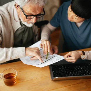 An elderly man and a healthcare worker review medicare advantage plan together at a table, both pointing to information on a document.