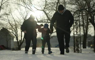 A mother and father walking with their child in a forested area in winter