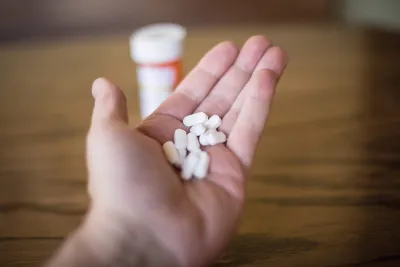 Hand holding pills with a pill bottle on the table nearby