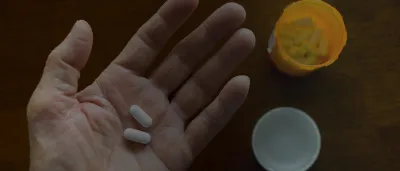 Hands holding two pills next to a pill bottle
