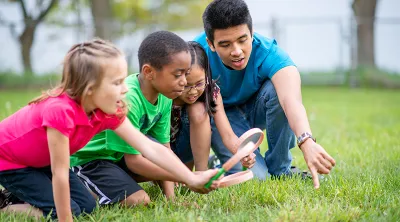 Group of kids looking in the grass with a magnifying glass