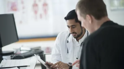 A doctor speaks with a person and points to a tablet device