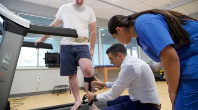 A man on a treadmill having his leg brace examined by two professionals