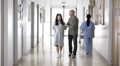 Pregnant couple walking down hospital hall with nurse