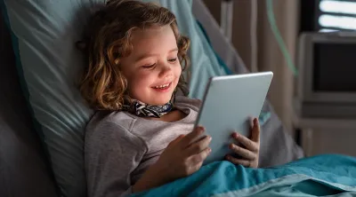 Young girl in a hospital bed reading a tablet computer