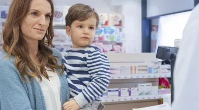 Mother holding child in checkout line at pharmacy counter. 