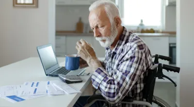 An elderly man looking at medical bills with a laptop computer