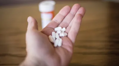 Hand holding pills with a pill bottle on the table nearby